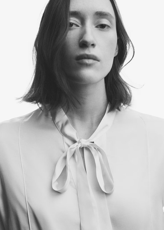 Mujer usando una camisa blanca coquette aesthetic con un lazo en el cuello.
