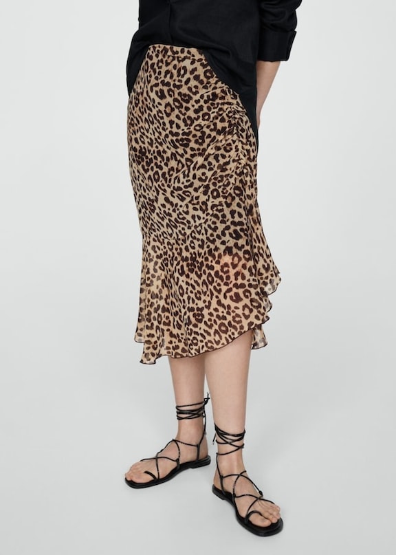 Donna che combina una gonna animalier con sandali e una camicetta nera.